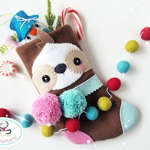 May include: A brown and white sloth-shaped Christmas stocking with a blue and white trim. The stocking is filled with a snowman ornament, candy canes, and pom-poms. A string of colorful felt balls is in the background.