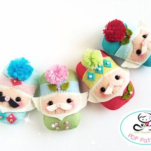 May include: Four felt ornaments shaped like people with colourful hats and beards. The ornaments are arranged in a row on a white background. The text "PDF Pattern" is visible in the bottom right corner of the image.
