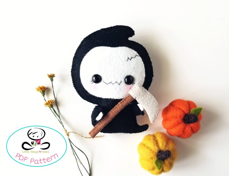 May include: A black felt plush toy of the Grim Reaper with a white face, holding a brown felt scythe. The toy is surrounded by two felt pumpkins, one orange and one yellow.