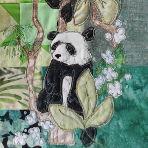 May include: Two embroidered panda bears climbing a tree branch with green leaves and white flowers. The pandas are white with black ears, eyes, and paws.