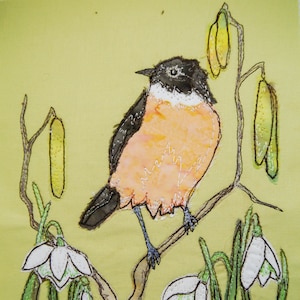 May include: A hand-stitched embroidery of a bird perched on a branch with white flowers. The bird has black and white feathers and an orange breast. The background is a light green.
