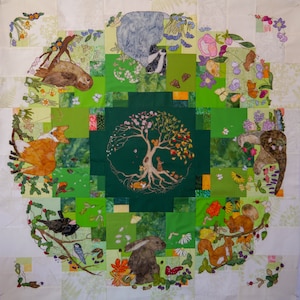 Könnte beinhalten: Eine grüne und braune Patchwork-Decke mit einem Lebensbaum-Design in der Mitte. Die Decke zeigt verschiedene Tiere, darunter einen Fuchs, ein Kaninchen, einen Dachs und ein Eichhörnchen. Die Decke ist von einem Rand aus Blumen und Blättern umgeben.
