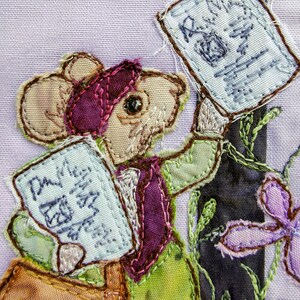 May include: A whimsical patchwork mouse holding two letters, one that says "Dear Me" and the other that says "Rain Mail". The mouse is wearing a purple hat and a green waistcoat. The background is a purple fabric with green and purple flowers.