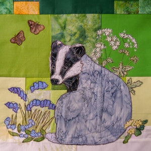 Könnte beinhalten: Eine Patchwork-Decke mit einem gestickten Dachs, Schmetterlingen und Blumen. Der Dachs ist grau und weiß, die Blumen sind blau und gelb.