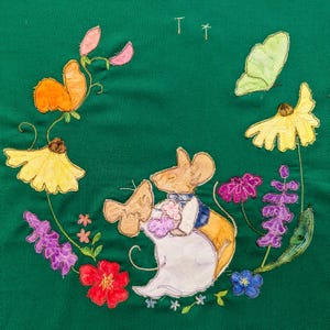 Könnte beinhalten: Ein grüner Stoff mit gestickten Blumen, Schmetterlingen und zwei Mäusen. Die Mäuse halten sich an den Händen und sind in ein weißes Kleid und eine blaue Weste gekleidet. Der Stoff ist mit verschiedenen Blumen verziert, darunter gelbe, lila und rote.