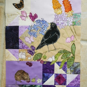 May include: A purple, green, and white patchwork quilt with embroidered images of a blackbird, a butterfly, flowers, and a mouse. The quilt is made of different fabrics and textures.