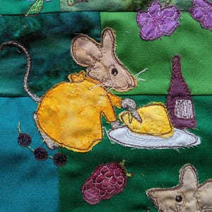 Könnte beinhalten: Eine gelbe Maus mit braunen Ohren und einem langen Schwanz hält ein Stück Käse auf einem weißen Teller. Die Maus sitzt auf einem grünen Stoffhintergrund mit einer lila Blume und einer Weinflasche.