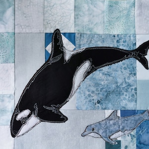 May include: A black and white orca whale and a grey dolphin embroidered on a blue and white patchwork fabric.