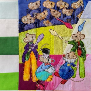 Könnte beinhalten: Ein farbenfroher, gesteppter Wandbehang mit einer Gruppe von Mäusen, die in einem Zirkus auftreten. Die Mäuse sind in verschiedenen Kostümen gekleidet und jonglieren, spielen Musik und führen andere Zirkusnummern auf. Der Hintergrund ist ein Patchwork aus verschiedenen Stoffen, darunter Blau, Grün, Gelb und Rosa.