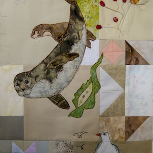 May include: A beige fabric quilt with embroidered images of seals, a jellyfish, a seagull, and a plant. The quilt is made up of different fabric squares in various shades of beige, brown, white, and pink.