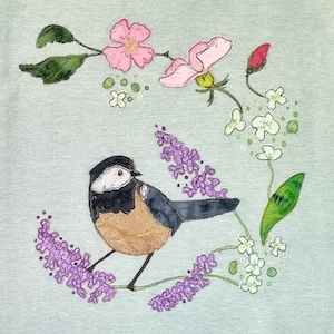 以下が含まれることがあります： 紫と白の花が咲いた枝に、黒い頭と茶色の胸を持つ青い鳥がとまっている。鳥は緑の葉とピンクの花に囲まれている。