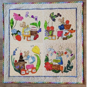 May include: A quilted wall hanging featuring four panels, each depicting a mouse engaged in baking activities. The panels are surrounded by floral and food illustrations, with a colorful border. The overall design is whimsical and charming.
