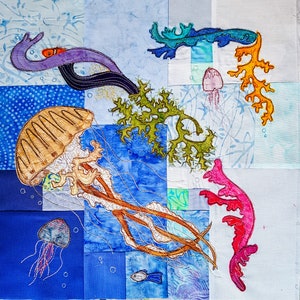 Peut inclure: Une œuvre d'art murale brodée colorée représentant une méduse, des algues et d'autres créatures marines. L'œuvre est composée de différents carrés de tissu cousus ensemble.