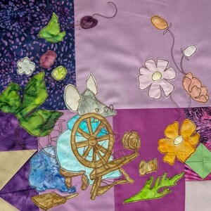 May include: A colorful patchwork quilt featuring a whimsical design. The quilt showcases a mouse operating a spinning wheel, surrounded by floral and leaf appliqués in shades of purple, blue, green, and yellow. The quilt is a charming piece of textile art.