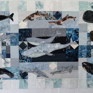 May include: A colorful patchwork quilt featuring various sea creatures, including a whale, orca, dolphins, and a sea turtle. The quilt is made of blue, gray, and white fabric.