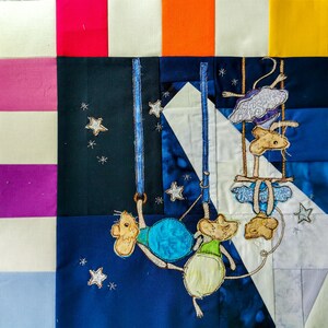 Könnte beinhalten: Ein Quiltblock mit dunkelblauem Hintergrund und weißen Sternen. Drei gestickte Mäuse hängen an blauen Seilen, eine Maus hält eine blaue und türkisfarbene Kugel. Der Quiltblock ist von einem Patchwork aus weißen, orangen, gelben, rosa und violetten Stoffen umgeben.