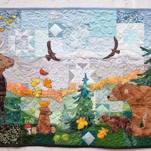May include: A colorful quilt featuring a moose, two bears, and a variety of trees and foliage. The quilt is made up of patchwork squares in shades of blue, green, brown, and yellow.