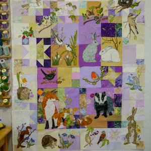 May include: A colourful quilt with a patchwork design featuring various animals, including rabbits, foxes, badgers, birds, and hedgehogs. The quilt is made with a variety of fabrics in shades of purple, brown, beige, and white.
