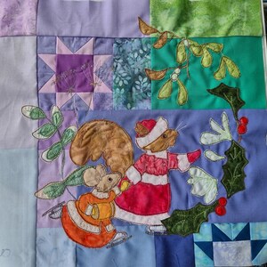 Könnte beinhalten: Ein gequilteter Wandbehang aus Stoff mit einem gestickten Design eines Eichhörnchens und einer Maus, die Schlittschuh laufen. Der Hintergrund ist ein Patchwork aus verschiedenen Stoffen in verschiedenen Farben, darunter Lila, Blau, Grün und Weiß.
