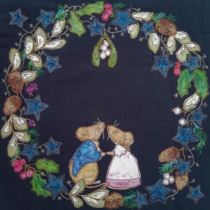 Könnte beinhalten: Ein schwarzer Stoffhintergrund mit einem Kranz aus grünen Blättern, blauen Sternen und braunen Beeren. Zwei gestickte Mäuse küssen sich in der Mitte des Kranzes.