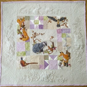 Könnte beinhalten: Ein weißer gesteppter Stoff mit rosa Rand zeigt ein Patchwork-Design mit verschiedenen Waldtieren, darunter ein Dachs, ein Fuchs, Eichhörnchen, Vögel und ein Fasan. Die Tiere sind in Braun-, Orange- und Grüntönen gestickt.