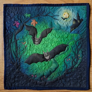 Peut inclure: Une tenture murale matelassée sur le thème d'Halloween représentant deux chauves-souris en vol sur un fond vert et bleu. Une pleine lune et la silhouette d'un château sont visibles en haut à droite. L'œuvre est encadrée d'une bordure bleu foncé.