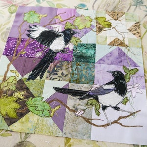 May include: A patchwork quilt with a floral design and two embroidered magpies. The quilt is made of various fabrics in shades of purple, green, and brown.