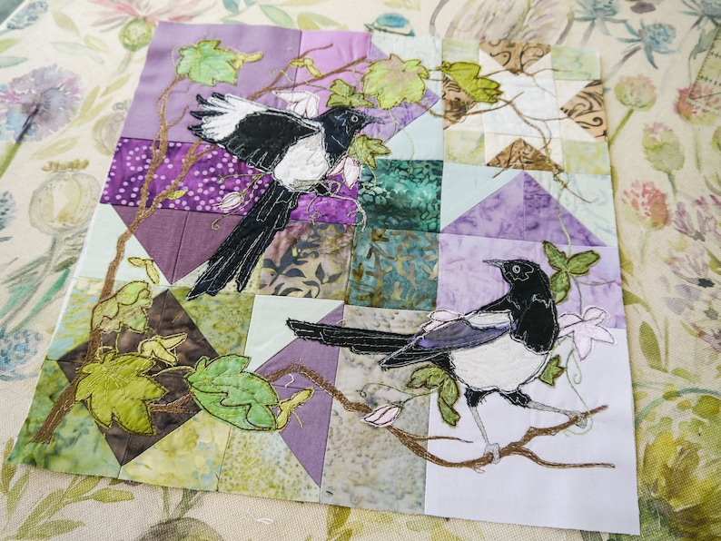 May include: A patchwork quilt with a floral design and two embroidered magpies. The quilt is made of various fabrics in shades of purple, green, and brown.