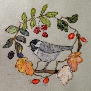 Peut inclure: Broderie représentant un oiseau gris perché sur une branche avec des feuilles vertes, des baies rouges et des feuilles d'automne orange et jaunes.