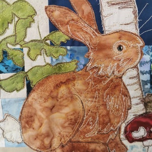 May include: A brown rabbit with white fur around its face and ears is sitting in a patch of green leaves. The rabbit is surrounded by a white, blue, and green patchwork background.