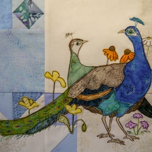 Könnte beinhalten: Ein blauer und grüner Pfau mit einem langen Schwanz und ein brauner und grüner Pfau mit einem kürzeren Schwanz. Die Pfauen sind auf einem weißen Stoffhintergrund mit gelben Blumen gestickt.