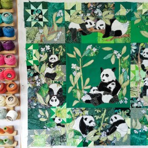 May include: A green and black patchwork quilt featuring a panda bear theme. The quilt depicts multiple pandas in various poses, including a mother panda with her cub, and a panda climbing a bamboo stalk. The quilt is made up of different fabric squares, each with a unique design.