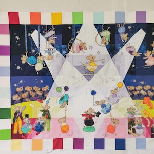 May include: A rectangular fabric quilt featuring a circus scene with multiple mice performing acrobatics, juggling, and balancing. The central design is framed by a colorful border of small squares in various hues, set against a dark blue starry sky.