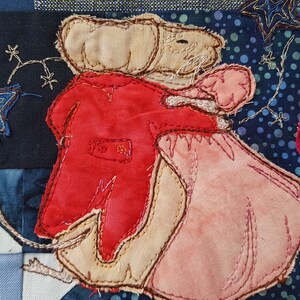 May include: A pair of embroidered fabric figures, a mouse in a red coat and a mouse in a pink dress, dancing together against a blue and white background.