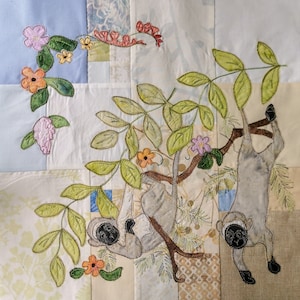 May include: Two embroidered monkeys hanging from a tree branch with green leaves and pink, orange, and yellow flowers. The monkeys are gray with black eyes and black noses.