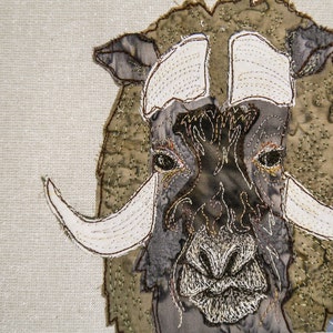 May include: Close-up of a brown and white embroidered musk ox with white horns. The musk ox is stitched on a beige fabric background.