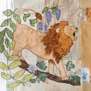May include: A beige lion with a brown mane stands on a branch with green leaves. The lion is embroidered on a beige fabric with a light brown background. The lion is looking to the right with its mouth open.