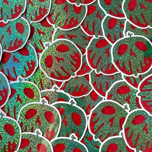 May include: A close-up of a collection of green and red glitter stickers featuring a skull and crossbones design. The stickers are arranged in a random pattern and are all slightly different in size and shape.