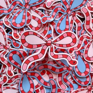 May include: A close-up of a pile of pink and blue worm-shaped stickers with a red and white bow design. The stickers are arranged in a random pattern.