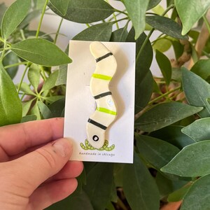 May include: A white ceramic worm with black and green stripes. The worm is depicted eating smaller green worms. The text "handmade in chicago" is printed on the card.