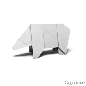 Puede incluir: Oso de origami blanco, doblado de una sola hoja de papel. El oso está de pie sobre una superficie blanca.