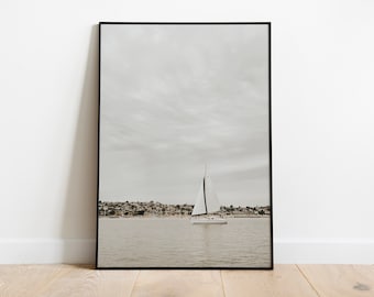 May include: A framed photograph of a sailboat on the water with a city skyline in the background. The sky is cloudy and the water is calm.