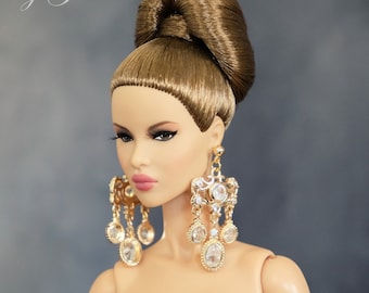 May include: A doll with long brown hair styled in a high bun, wearing a white strapless dress and large gold earrings with clear crystals.