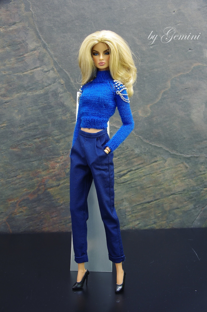 May include: A blue knitted sweater with silver embellishments on the shoulders, paired with dark blue pants and black heels.