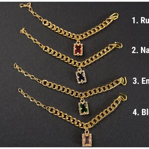 May include: Gold-toned chain jewelry with rectangular gemstone pendants in ruby, navy, emerald, and blush pink. The image shows four pieces of jewelry with different colored gemstones, each labeled with a number and color name.