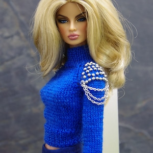 May include: A blue knitted sweater with a silver chain and studded detail on the shoulder. The sweater has a high neck and long sleeves.
