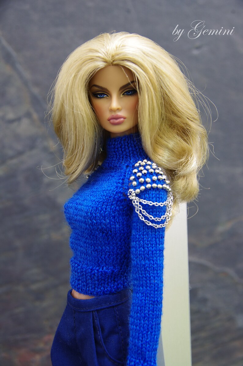 May include: A blue knitted sweater with a silver chain and studded detail on the shoulder. The sweater has a high neck and long sleeves.