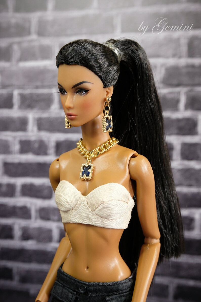 May include: A fashion doll with long black hair in a high ponytail, wearing a cream-colored bustier, and dark denim pants. The doll is accessorized with a gold chain necklace and matching earrings, each featuring a dark blue square pendant. The image is signed "by Gemini".