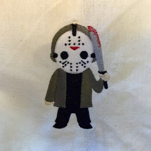 May include: Embroidered patch featuring a cartoon version of Jason Voorhees from the Friday the 13th horror film series. The patch shows Jason wearing his signature hockey mask and holding a bloody machete. The patch is on a white background.