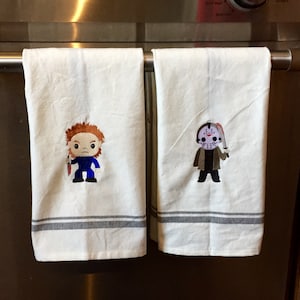 May include: Two white kitchen towels with gray stripes and embroidered horror movie character designs. One features a character with red hair and a knife, the other a masked figure with a machete.